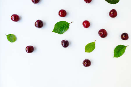 Bright red juicy ripe cherry with green leaves scattered on a white background. High quality photoの写真素材