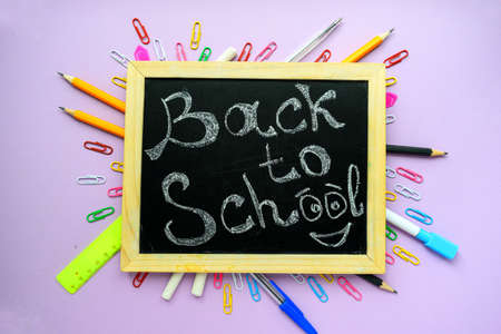 Back to school text on a black school board with a wooden frame on a purple background and...