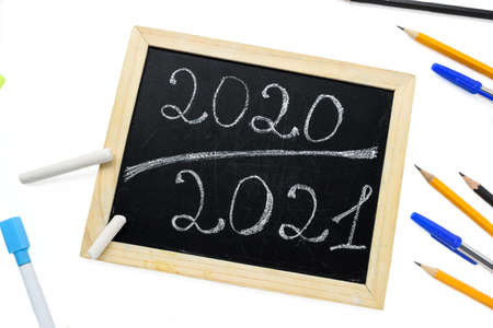 Inscription 2020 2021 chalk on a black board with a wooden frame on a white background with stationery. High quality photoの写真素材