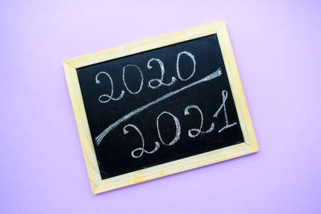 Inscription 2020 2021 on a black chalkboard chalked by hand on a purple background with a wooden frame. High quality photoの写真素材