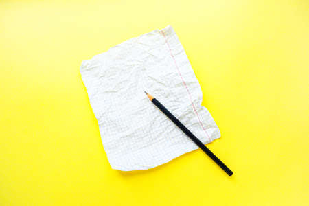 A white sheet of notebook paper in a cage on a bright yellow background with a black slate pencil. . High quality photoの写真素材