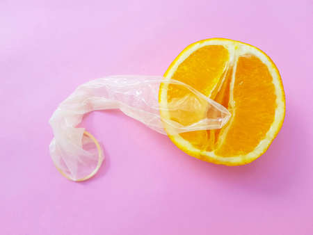 The concept of safe sex and protection. A vagina symbol. A juicy orange and a condom on a bright...