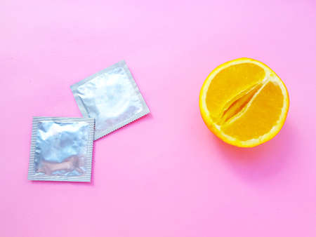 The concept of safe sex and protection. A vagina symbol. A juicy orange and a condom on a bright pink background. High quality photoの写真素材