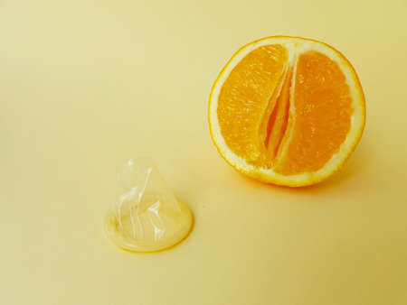 The concept of safe sex and protection. A vagina symbol. A juicy orange and a condom on a bright yellow background. High quality photoの写真素材