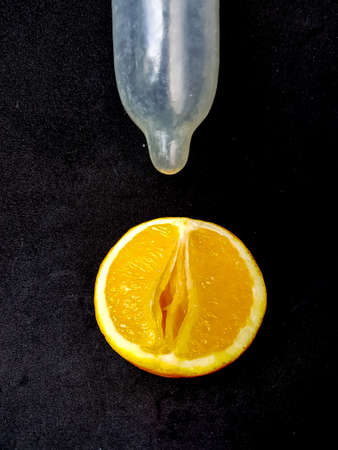 The concept of safe sex and protection. A vagina symbol. A juicy orange and a condom on a black background. High quality photoの写真素材