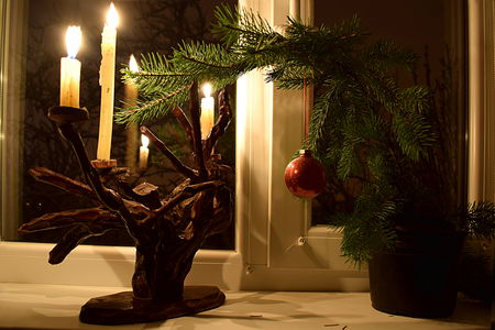 On the windowsill there is a candlestick with lit candles, which illuminate a decorated branch of a Christmas tree.の写真素材