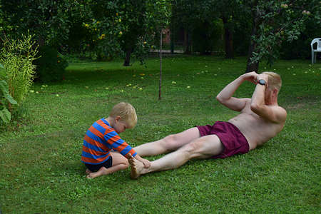 The little son helps his father do exercises to strengthen the abdominal muscles.の写真素材