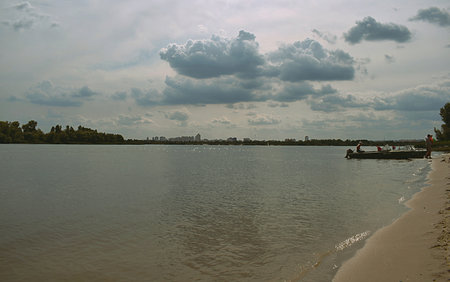 Landscape: sandy river bank with a moored boat, Kiev city on the horizon.