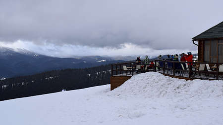 People are resting in a cafe with a viewing platform in a ski resort.