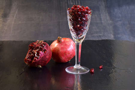 Pomegranate fruits and pomegranate seeds in a glass on a black background.の写真素材