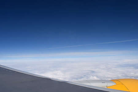 View from the porthole of an airplane flying above the clouds. In the distance, the condensation...
