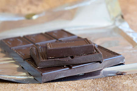 A bar of dark chocolate on packaging foil close-up.