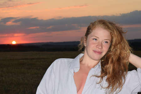 Portrait of a young woman in front of a mowed field at sunset.