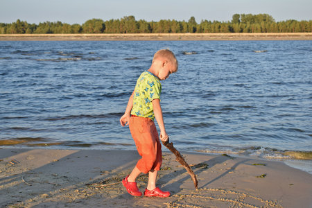 A boy draws on the wet beach sand with a stick.の写真素材