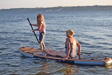Granddaughter rides grandmother on a sup board on the lake.の写真素材