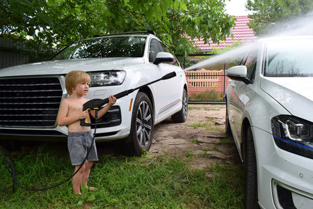 A little boy is washing a car with a pressure washer.の写真素材
