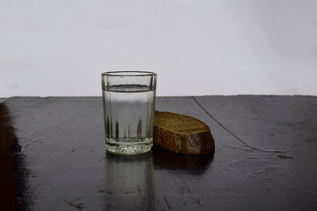 A glass of water and a loaf of black bread on a black table.の写真素材