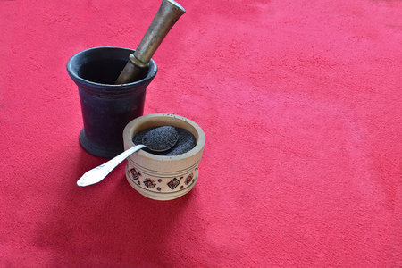 Poppy seeds in a wooden cup and mortar with pestle on a red background.