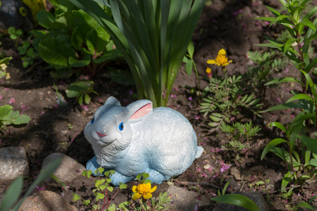 garden figurine of a rabbit sitting under a bushの写真素材