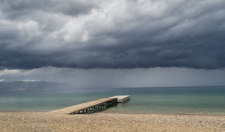Heavy dark clouds above blue lake with wooden dock in itの写真素材