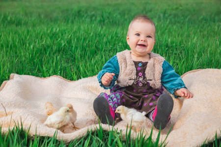 baby in a colorful dress on the lawn with chickensの写真素材