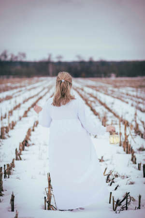 Attractive woman in nightgown in the field in winter with hand lampの写真素材