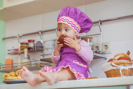 beautiful baby in an apron eating honey on the kitchen tableの写真素材