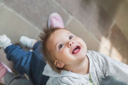 beautiful toothless baby leaned back holding mom's hands