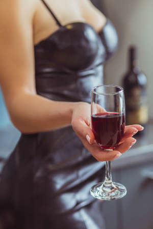 slim woman in a leather dress holds a wineglass with red wineの写真素材