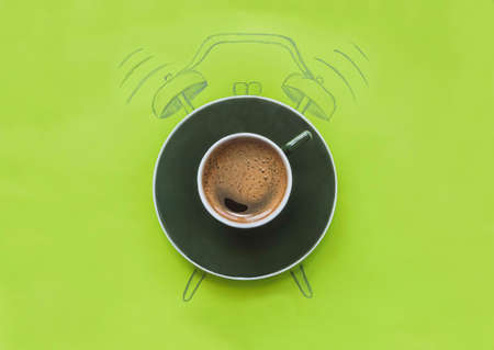 a cup of coffee stands on a drawn alarm clock on a green background