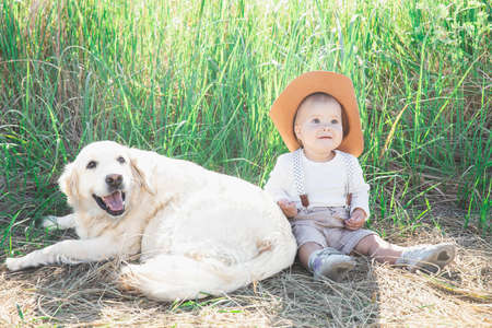 beautiful blond baby in a suit with suspenders sits in the grass with dog