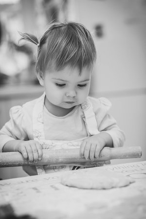 Adorable baby in an apron is rolling out the dough in the kitchenの写真素材