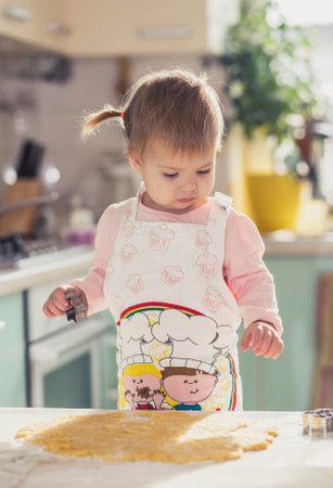 Adorable baby in an apron makes cookies from dough in the kitchenの写真素材