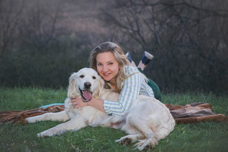 attractive blonde hugging with dog on a plaid in the forest in the eveningの写真素材