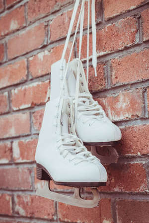 White figure skating skates hang on a brick wall in a barnの写真素材