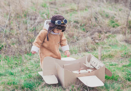 Charming baby in aviator's clothes gets on the cardboard planeの写真素材