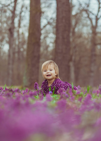 blond baby in a colored dress lies in a forest glade in flowersの写真素材