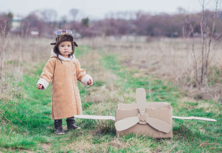 Charming baby in aviator's clothes stands near a cardboard planeの写真素材