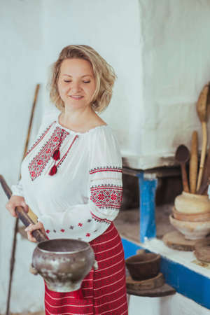 Hostess in embroidered clothes pulled a pot of food out of the oven. Retro photo of ancient Ukrainian lifeの写真素材
