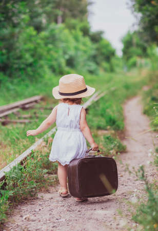 Charming baby with a suitcase walks along the railroadの写真素材