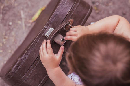 Adorable baby trying to open a suitcase with a hair clipの写真素材