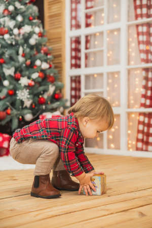 cute baby in trousers and a plaid shirt plays on the floor with wooden cubeの写真素材