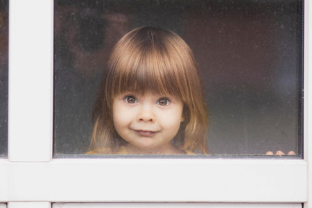 Beautiful fair-haired baby looking out the windowの写真素材