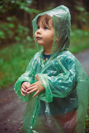 Charming child in a raincoat in the evening forest in Denmarkの写真素材