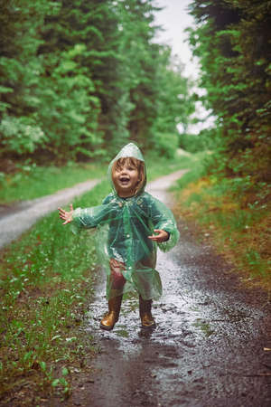Charming child in a raincoat in the evening forest in Denmarkの写真素材