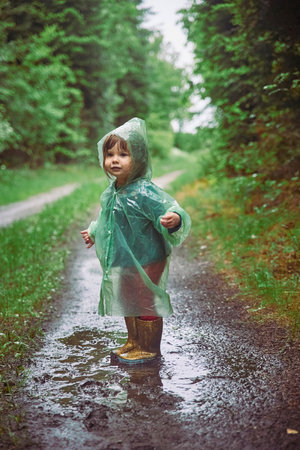 Charming child in raincoat in the evening forest in Denmarkの写真素材