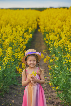 charming child in sundress in a rapeseed fieldの写真素材