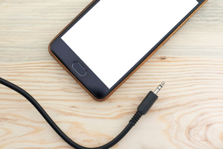 Mobile phone and audio wire on wooden background close upの写真素材