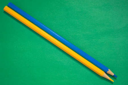 Blue and yellow pencils lying on a green background closeupの写真素材