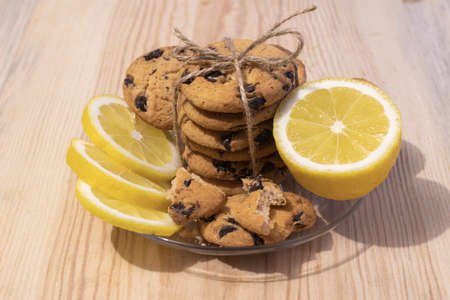 Shortbread cookies with pieces of chocolate tied with twine and lemon on a glass plate, on a wooden background close-upの写真素材